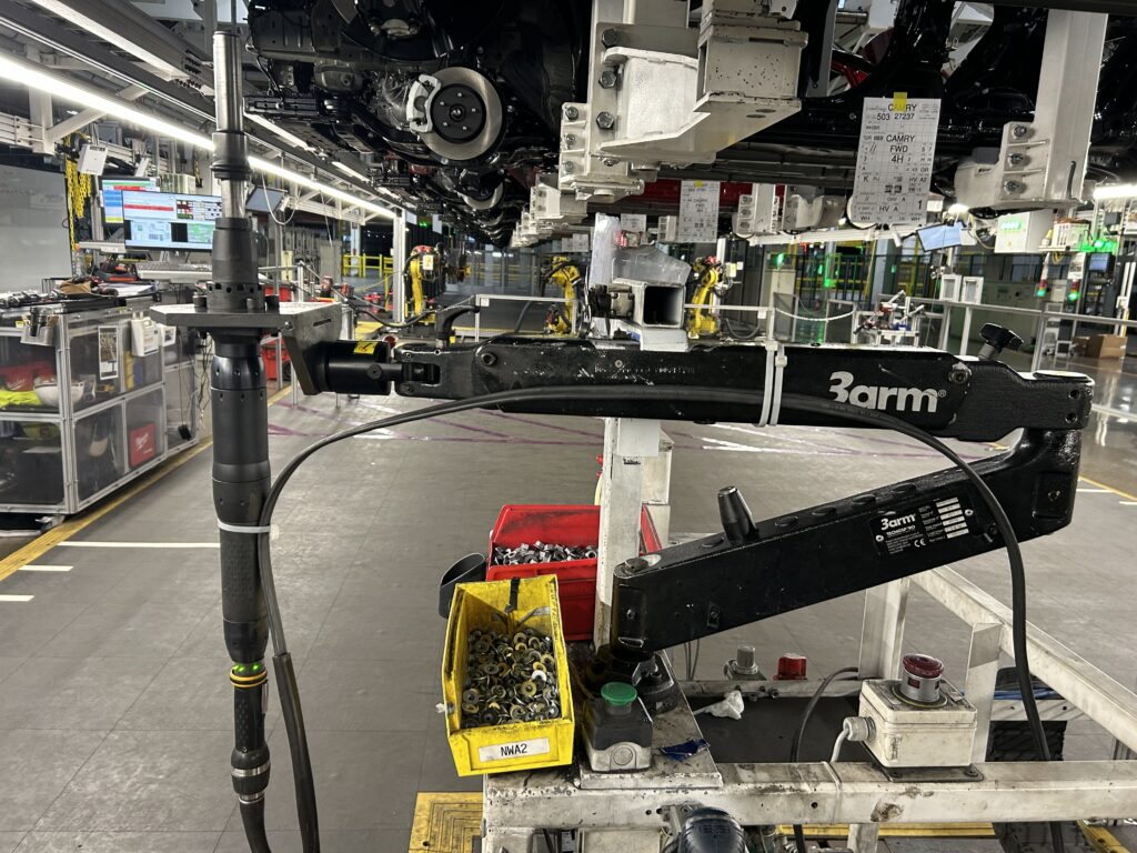 Opérateur utilisant un bras articulé industriel équipé d'un équilibreur de charge pour manipuler une meuleuse en hauteur dans une usine de fabrication